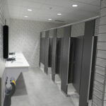 Public restroom with a row of sinks along the left wall and gray stall doors on the right side of the room.