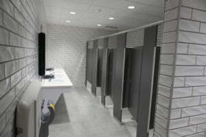 Public restroom with a row of sinks along the left wall and gray stall doors on the right side of the room.