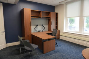 Office workspace with navy accent wall, a large wood desk and built-in wall cabinets, and two adjustable desk lamps facing forward.