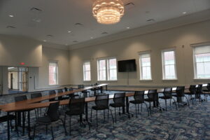 Large conference room with long wooden tables arranged in rows, black chairs, and a decorative chandelier overhead.