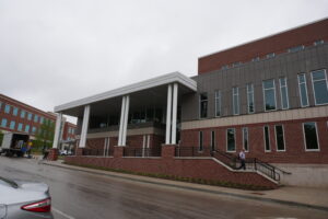Modern brick campus building with a white portico supported by columns and large windows along the facade, street in foreground.