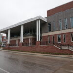 Modern brick campus building with a wide covered entrance supported by white columns and tall vertical windows on the right.