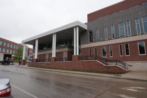 Modern brick campus building with a wide covered entrance supported by white columns and tall vertical windows on the right.