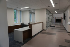 Reception desk in a modern office with a marble-pattern front, dark wood cabinets, and two black mesh chairs. Large windows line the left wall, bringing in light.