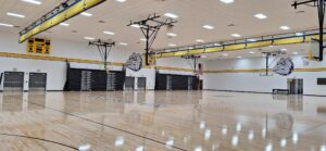 Empty school gym with basketball hoops, polished wooden floor, yellow/blue accents, and bulldog mascot decals on the walls.