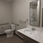 Accessible bathroom with a toilet and sink, equipped with multiple metal grab bars for accessibility and a large mirror above the sink.