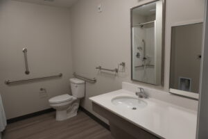 Accessible bathroom with a toilet and sink, equipped with multiple metal grab bars for accessibility and a large mirror above the sink.