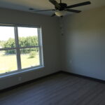 Empty room with a large window showing a green landscape outside; ceiling fan hangs from the ceiling.