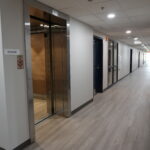 Hallway interior with a partly open elevator on the left and evenly spaced doors along the corridor.