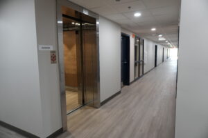 Hallway interior with a partly open elevator on the left and evenly spaced doors along the corridor.