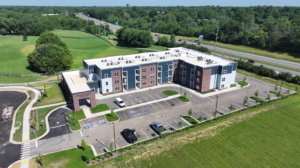 Aerial view of Wellington Park Apartments: a three-story brick-and-blue siding complex with a curved driveway and green surroundings.
