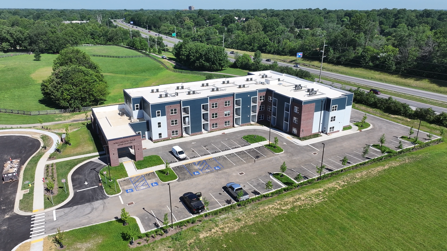 Aerial view of Wellington Park Apartments: a three-story brick-and-blue siding complex with a curved driveway and green surroundings.