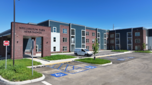 Exterior view of Wellington Park Apartments, brick and blue siding, with accessible parking spaces in the foreground.