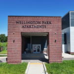 Front view of Willington Park Apartments with a brick entryway under a clear blue sky.