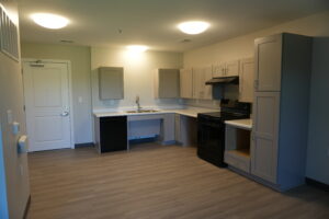 Modern L-shaped kitchen with gray cabinets, white countertops, stainless steel sink, and a black range stove with vent hood on the right.