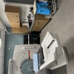 MRI scanner in a clinical imaging room with patient table and wooden cabinets along the wall