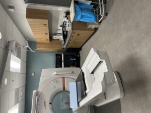 MRI scanner in a clinical imaging room with patient table and wooden cabinets along the wall