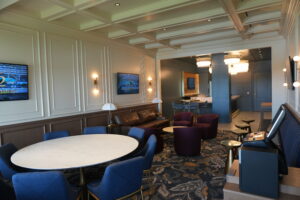 Spacious hotel lounge with round white tables, blue chairs, and purple ottomans along paneled beige walls.