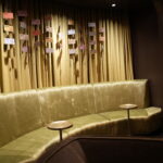 Gold velvet curved sofa in a dim lounge with small hanging tickets on a striped curtain backdrop