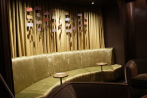 Gold velvet curved sofa in a dim lounge with small hanging tickets on a striped curtain backdrop