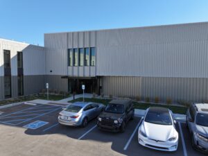 Exterior of a modern gray metal-clad building with vertical panels and large windows, under a clear blue sky.