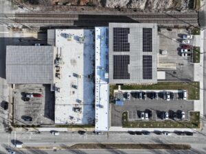 Aerial view of a commercial rooftop complex with solar panels, adjacent parking lots, and railway tracks nearby at the top of the image.