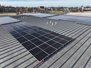 Rooftop view of multiple solar panels installed on a corrugated metal roof with an urban background.