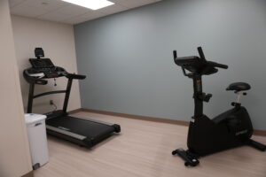 Small home gym with a treadmill on the left and a stationary bike on the right against pale blue walls and a tiled ceiling.