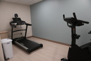 Treadmill against a light wall with a cardio bike partially visible in a small workout room.