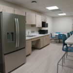 A modern break room with a stainless steel refrigerator, wooden cabinets, and a countertop along a wall with a sink and microwave.