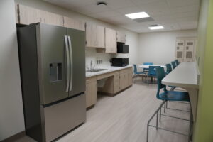 A modern break room with a stainless steel refrigerator, wooden cabinets, and a countertop along a wall with a sink and microwave.