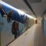 Long hallway with a colorful mural: blue sky, a soaring eagle, rockets, and cartoon characters along the walls.