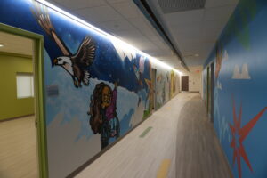 Long hallway with a colorful mural: blue sky, a soaring eagle, rockets, and cartoon characters along the walls.