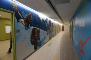 Colorful mural hallway with blue walls, cartoon characters, and a person entering from the left.