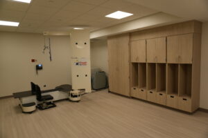 Clinic treatment room with medical equipment, a tall white cabinet, and wooden wall lockers; Kosair for Kids sign on the cabinet.