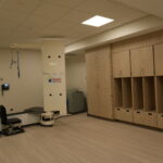 Clinical imaging room featuring a tall white medical device and row of wooden storage lockers along the wall, illuminated by ceiling lights