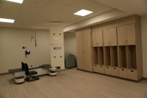 Clinical imaging room featuring a tall white medical device and row of wooden storage lockers along the wall, illuminated by ceiling lights