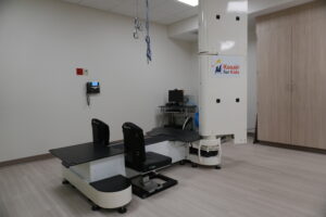 Medical imaging room with a large robotic X-ray table and overhead gantry; sign reads 'Kosair for Kids' on the machine column.