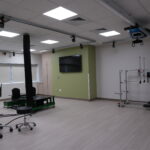 Rehabilitation lab with ceiling-mounted track system and robotic therapy devices, green accent wall and wall-mounted TV.
