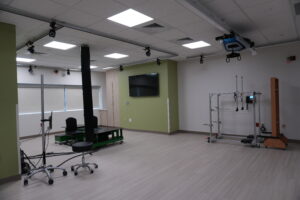 Rehabilitation lab with ceiling-mounted track system and robotic therapy devices, green accent wall and wall-mounted TV.