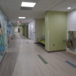 Hospital corridor with mural of a cyclist on the left, seating area on the right, and a water fountain visible in the distance.