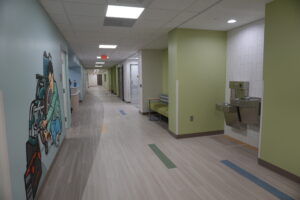 Hospital corridor with mural of a cyclist on the left, seating area on the right, and a water fountain visible in the distance.