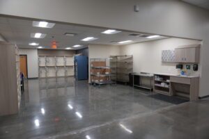 Empty supply room with beige walls, metal shelving, and cardboard boxes on a rolling rack.