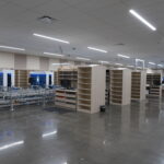 Large, empty industrial space with modular shelving and conveyor machinery set up, bright ceiling lights, and polished concrete floor.