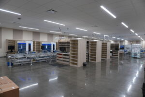 Large, empty industrial space with modular shelving and conveyor machinery set up, bright ceiling lights, and polished concrete floor.