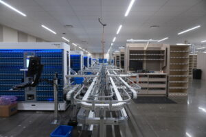 Automated conveyor system in a large warehouse with blue storage modules and empty shelves along the sides.