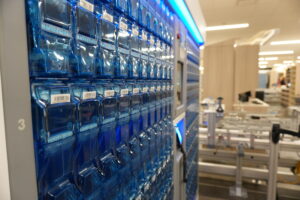 Row of blue plastic storage pockets with barcode labels mounted on a wall in a bright facility (warehouse/office).