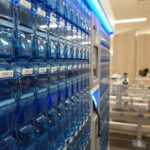 Blue vending cabinet filled with stacked clear blue capsules and barcode labels in a store setting.