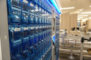 Blue vending cabinet filled with stacked clear blue capsules and barcode labels in a store setting.