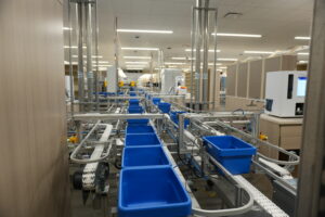 Automated warehouse conveyor line with blue plastic bins and metal framing in a fulfillment area.